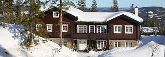 Et stort hus dekket av snø med trær i bakgrunnen