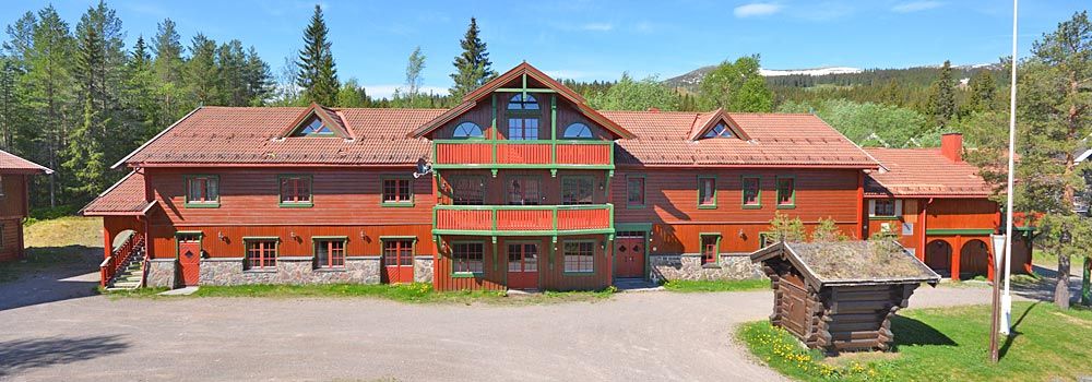 En stor rød bygning med rødt tegltak er omgitt av trær.