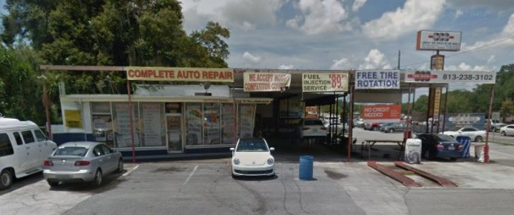 A low, single-story auto repair shop with multiple service bays, signage for repairs, and cars parked in front.