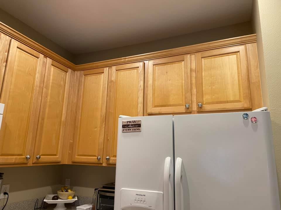 Light wood kitchen cabinets above a white refrigerator; beige walls.