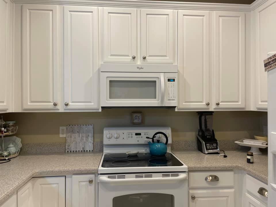 White kitchen with cabinets, microwave, stove, and countertop, a blue kettle, and a blender.