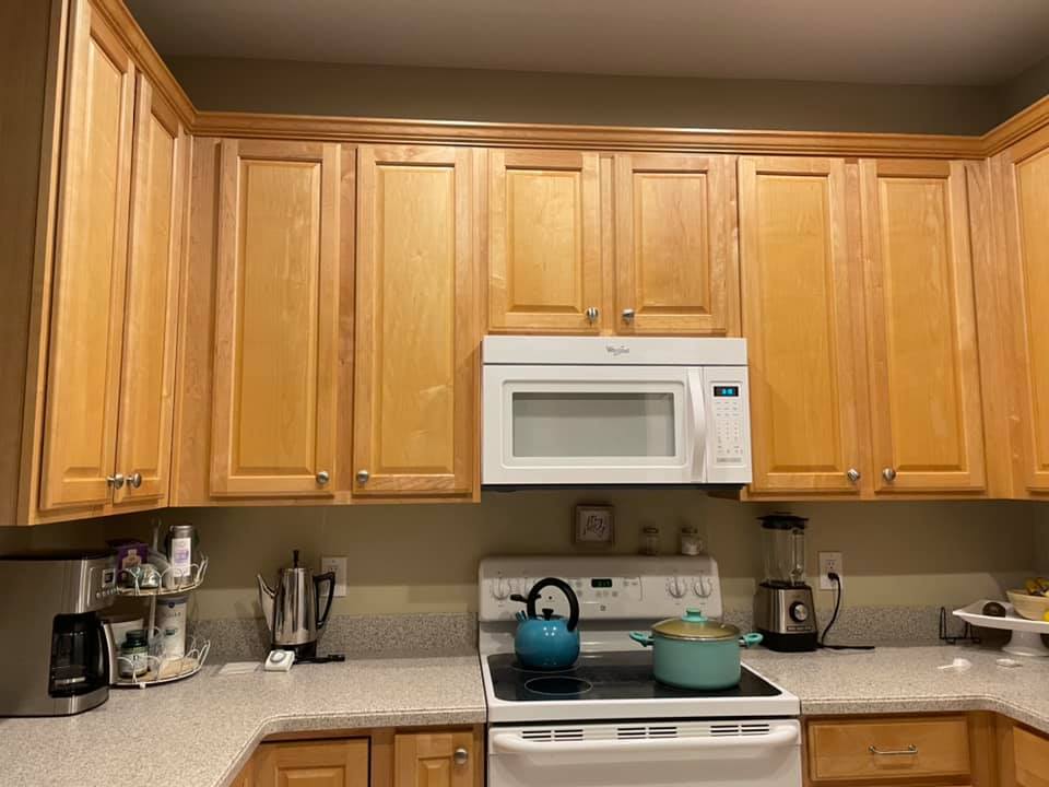 Kitchen with light-colored wood cabinets, white microwave over the stove, and various kitchen appliances.