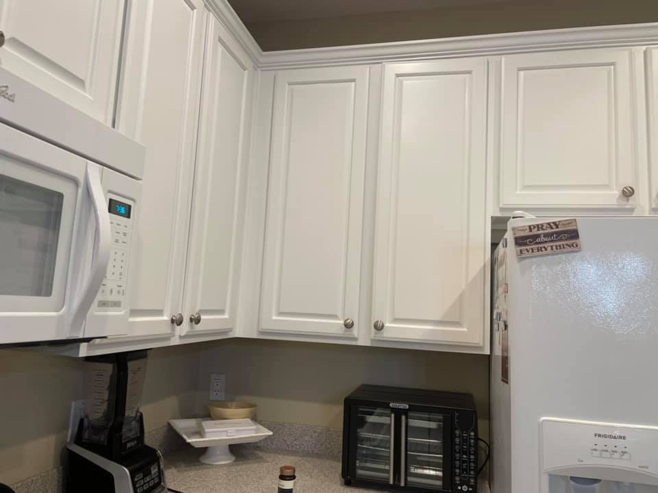 White kitchen cabinets with silver knobs and a white microwave above the countertop.