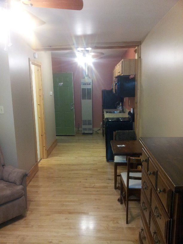 Narrow room with hardwood floors, a green door, and small kitchenette.