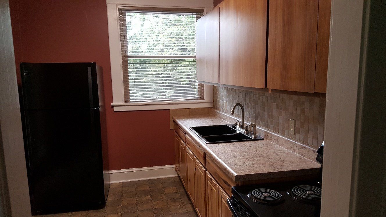Small kitchen with a black refrigerator, wooden cabinets, and a sink beneath a window.