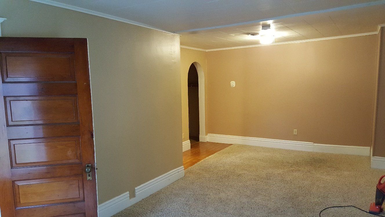 Interior room with tan walls, white trim, and a brown wooden door. Carpet and an arched doorway.
