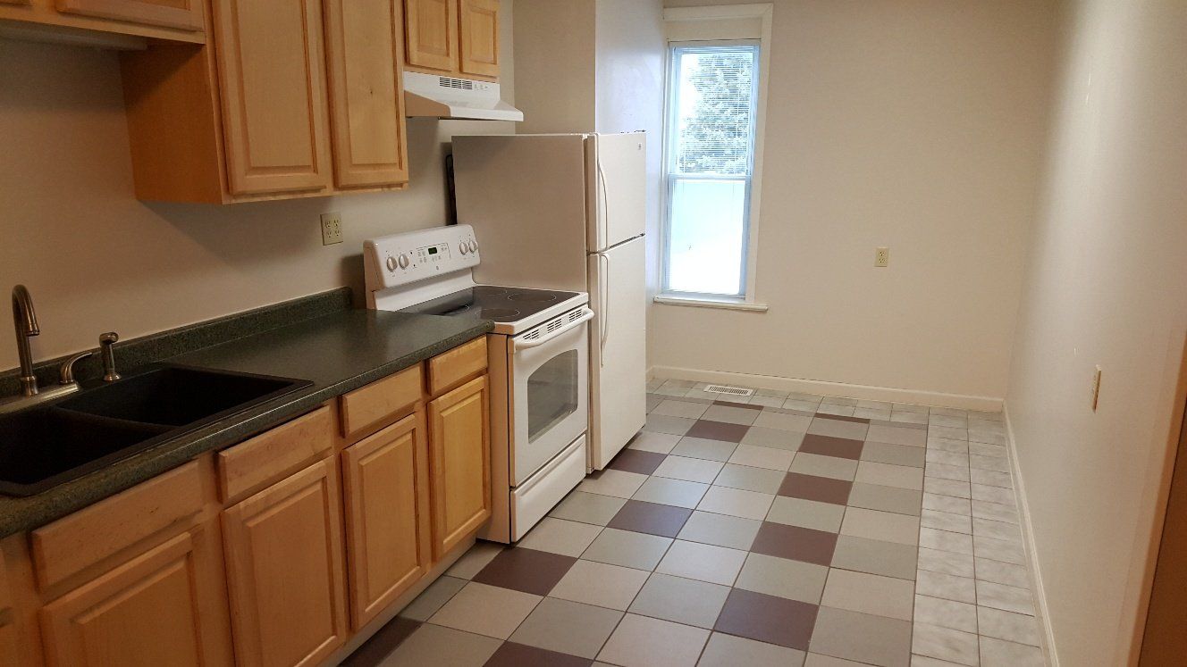 Kitchen with wood cabinets, dark countertop, white appliances, and checkered tile floor.