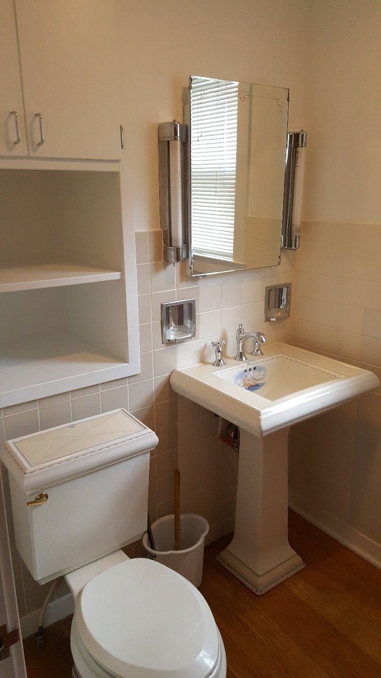 White bathroom with pedestal sink, toilet, and mirrored medicine cabinet.