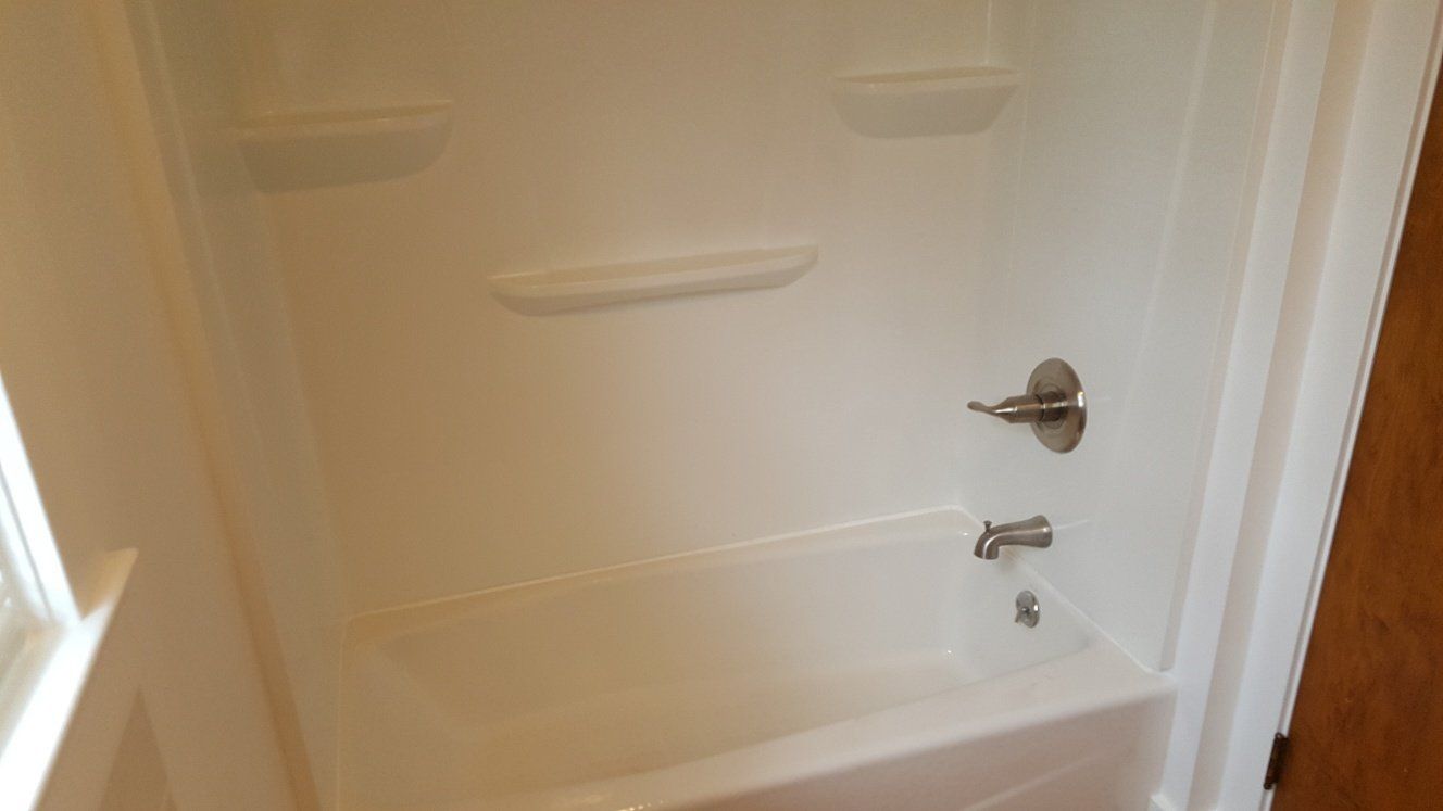White alcove bathtub with integrated shelves and chrome fixtures.