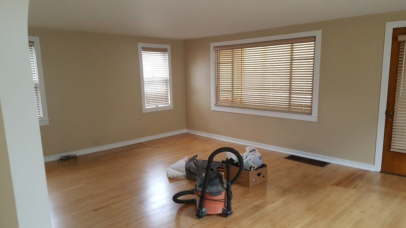 Empty room with tan walls, light wood floor, windows, and a vacuum cleaner.