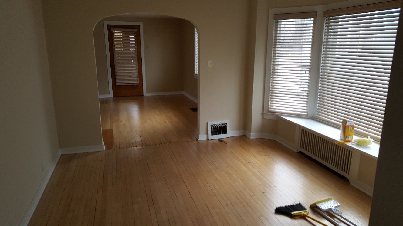 Empty room with hardwood floors, beige walls, arched doorway, and a bay window with blinds.