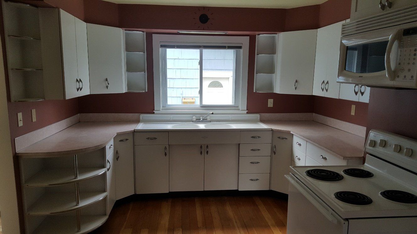 White kitchen cabinets with pink countertops against a red wall, with a stove and window.