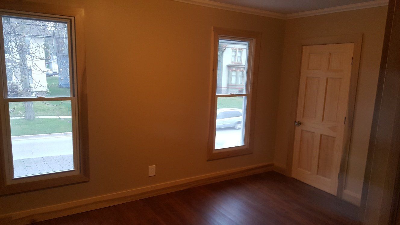 Empty room with two windows, a door, and wood floors. Walls are painted tan.
