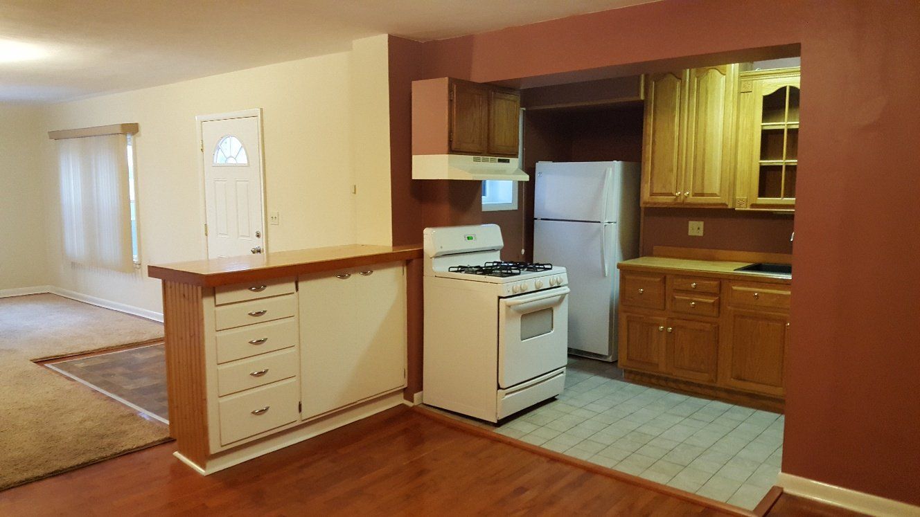 Open-concept kitchen and living area with white appliances, wooden cabinets, and a bar counter.
