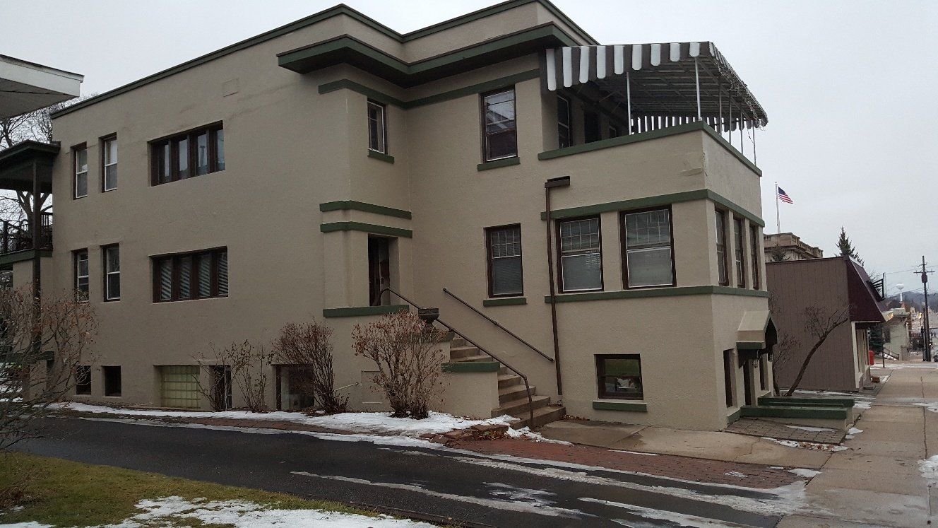 Multi-story tan building with green trim, steps, and awning. Snow on the ground.
