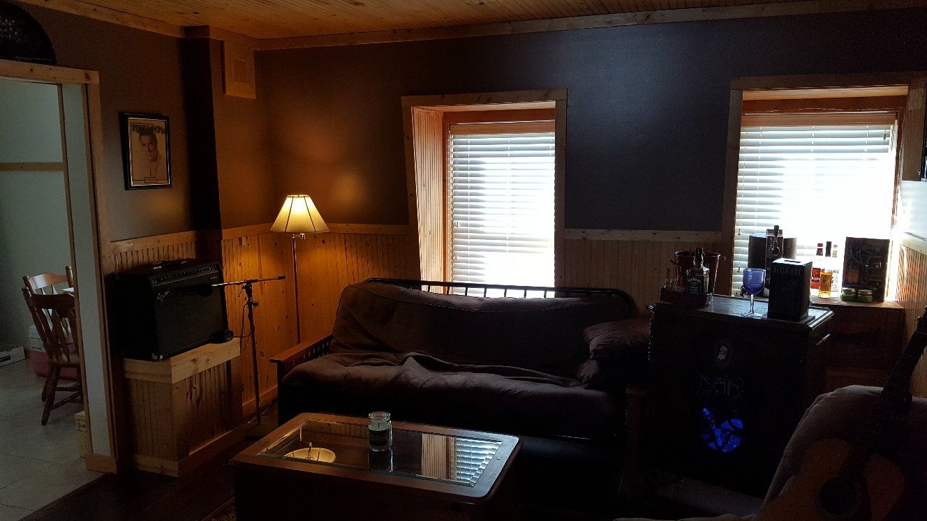 Cozy living room with dark gray walls, a sofa, coffee table, and windows with blinds. A floor lamp illuminates the space.