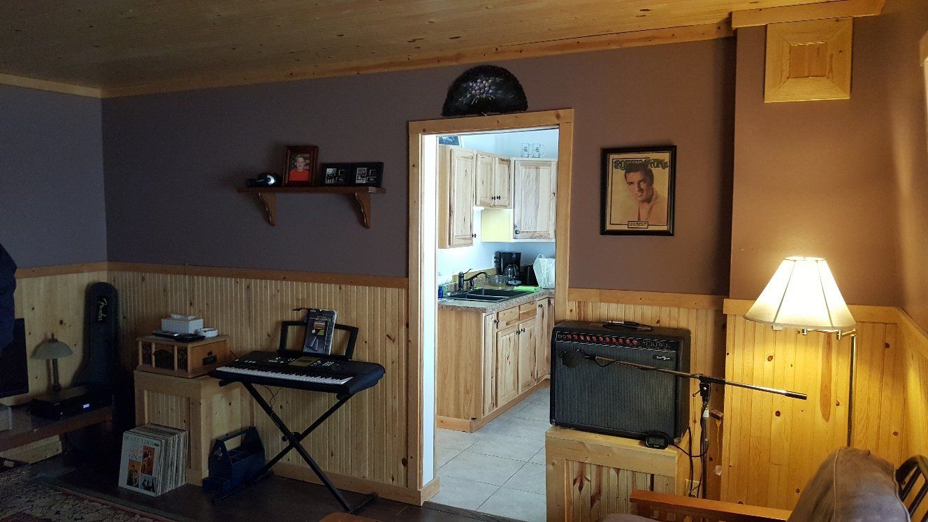 Room with purple walls, wood paneling, doorway to kitchen, keyboard, amp, and lamp.