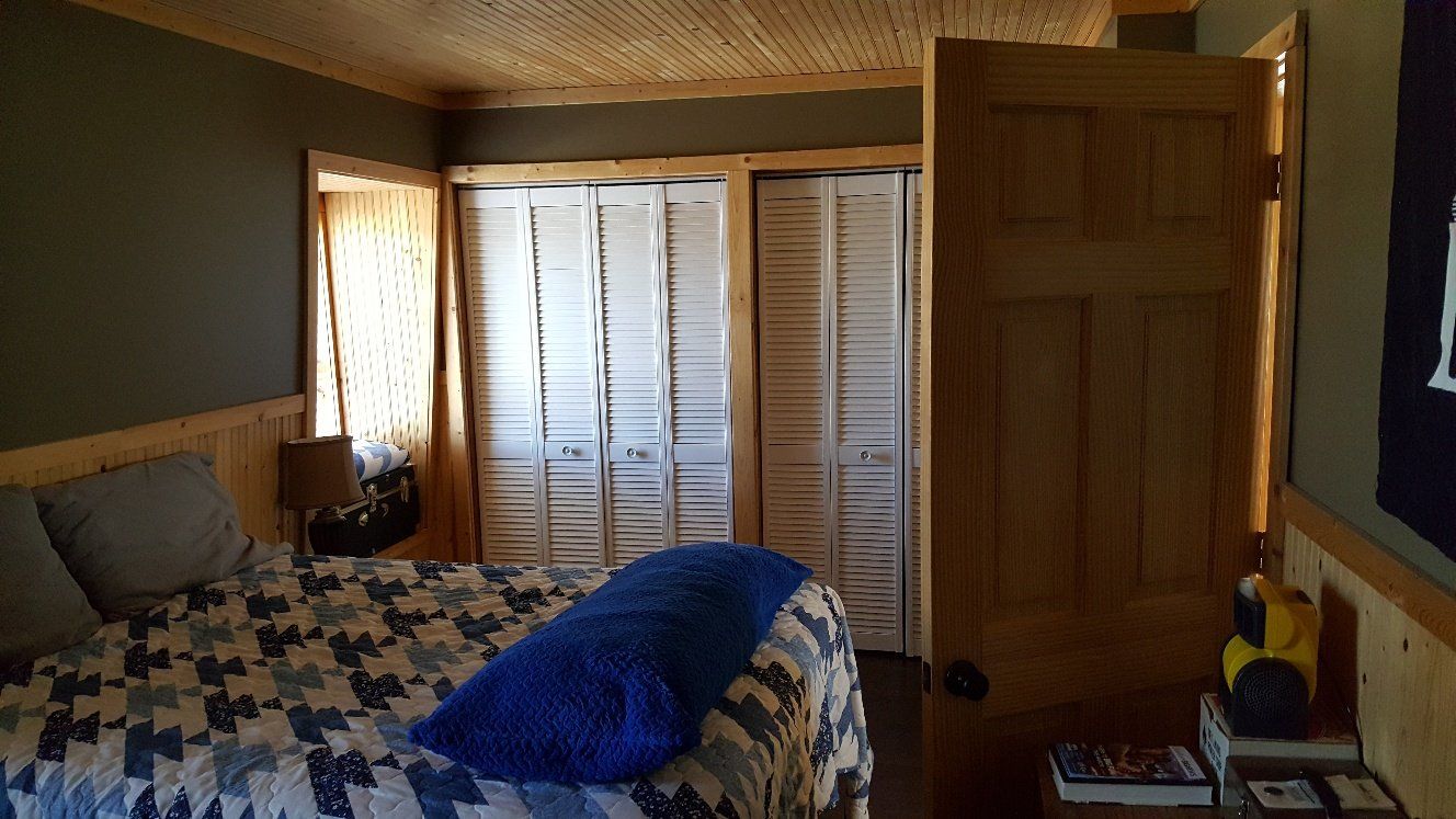 Bedroom interior with bed, wooden door, and closet with white shutters. Dark walls, wood trim.