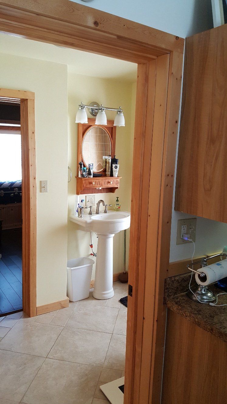 Bathroom interior with white pedestal sink, wooden mirror frame, and light fixture.
