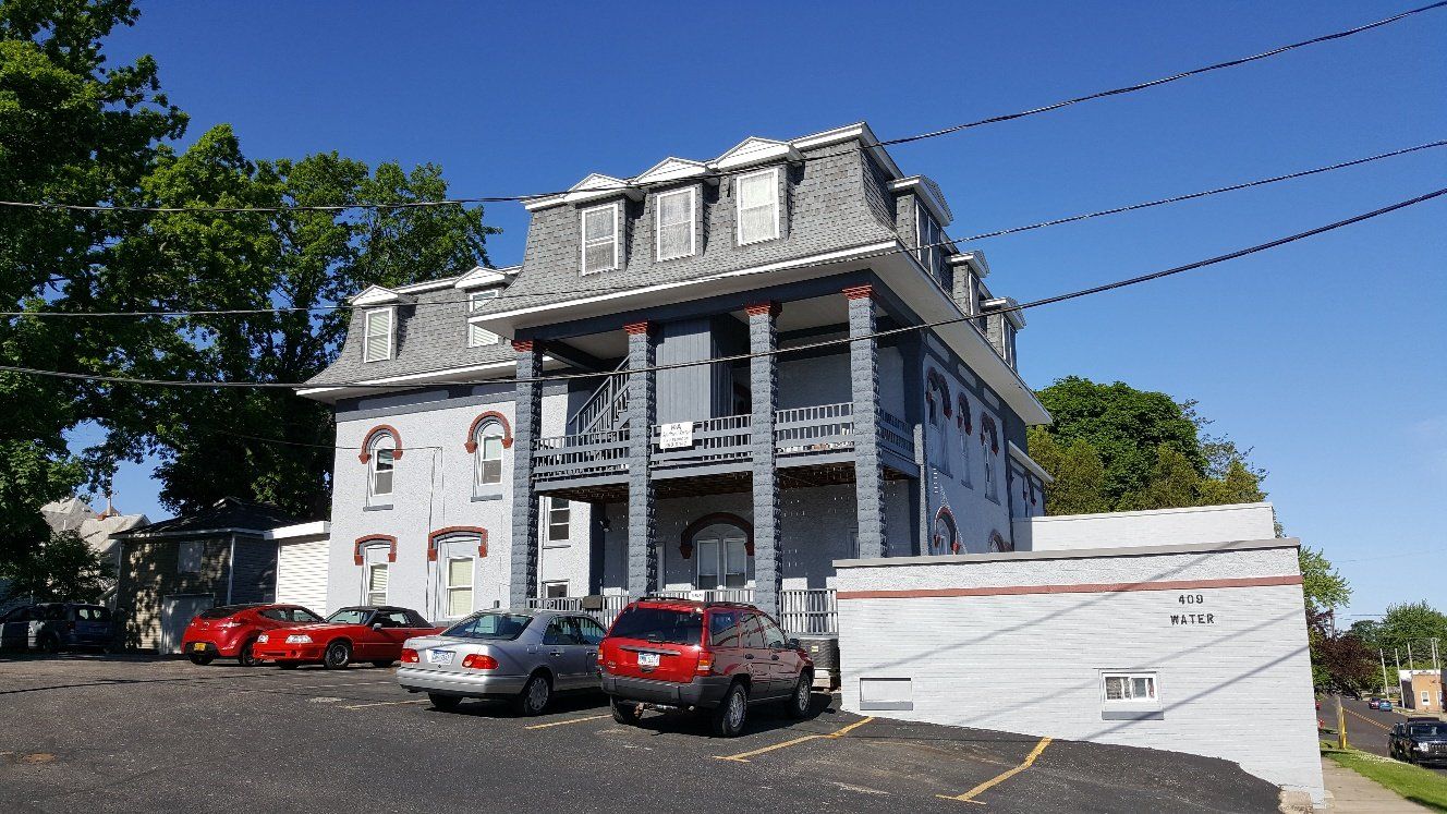 Gray and red multi-story building with cars parked in front.