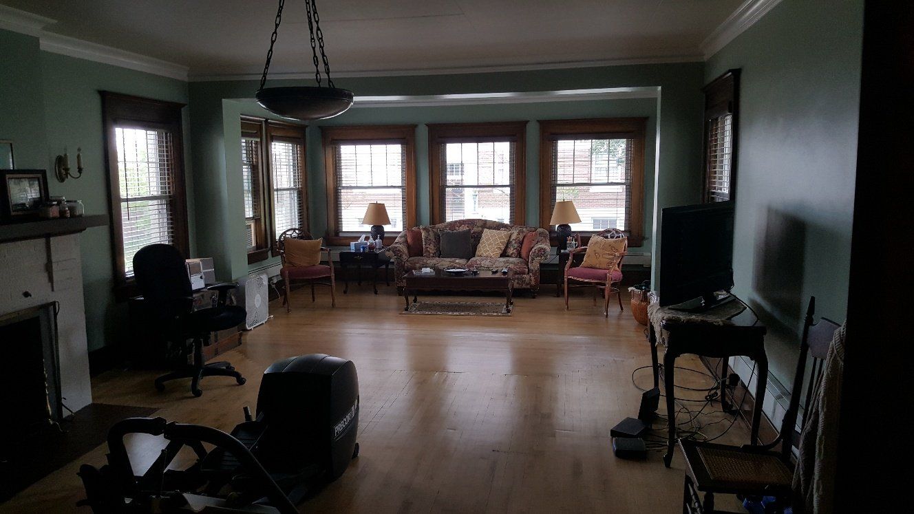 Spacious living room with hardwood floors, green walls, fireplace, and large windows. Furnishings are scattered.