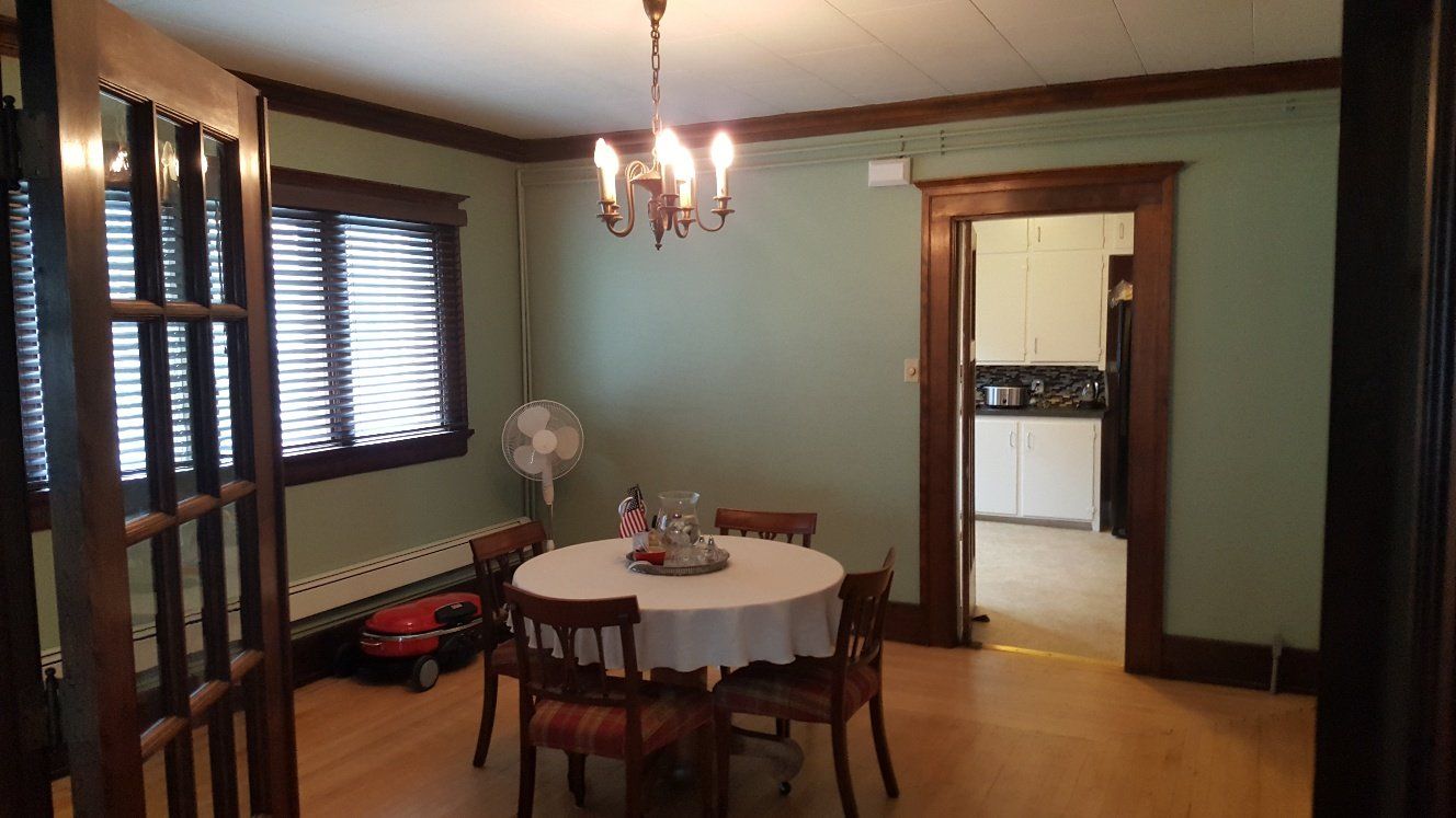 Dining room with round table set for four, green walls, dark wood trim, and a chandelier.