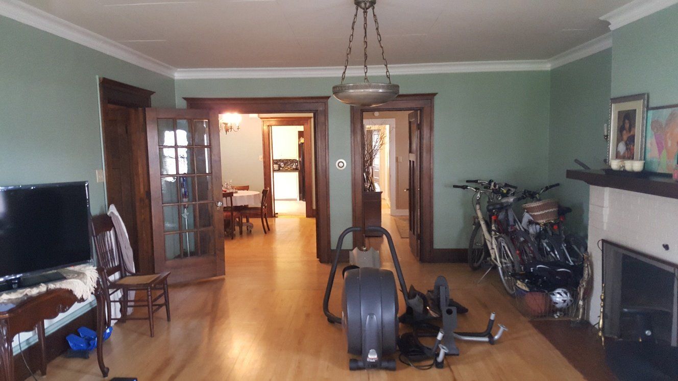Living room with hardwood floors, green walls, wooden trim, and an elliptical machine. Bikes and fireplace on right.