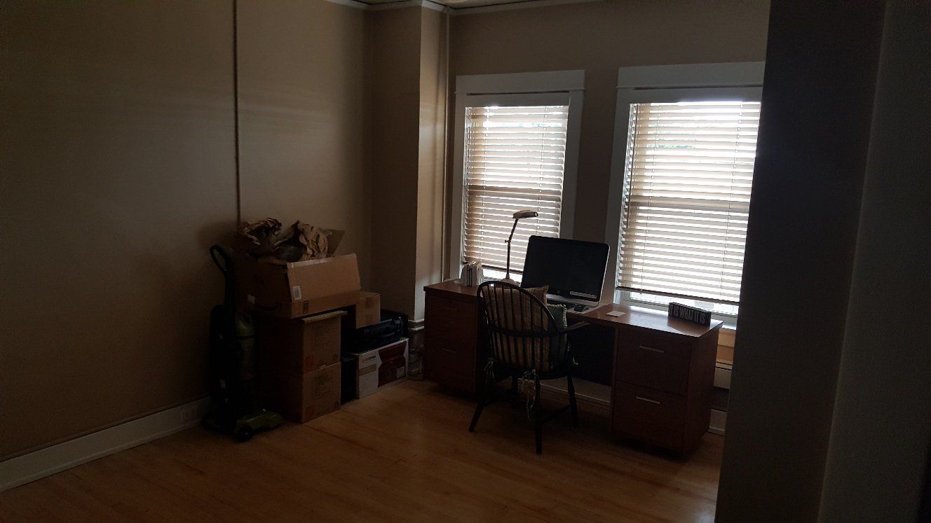 Room with desk, chair, computer, window, and boxes; wood floor and tan walls.