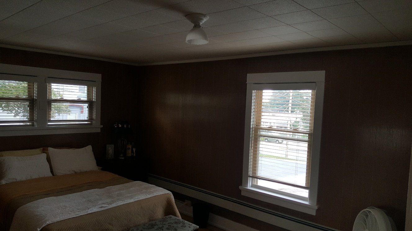 Bedroom with brown walls, two windows, bed with white pillows and a ceiling fan.