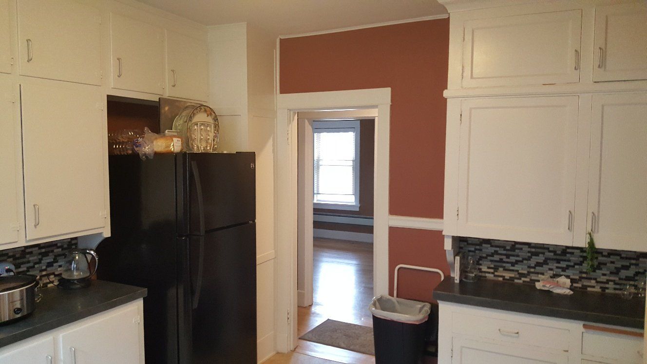 Kitchen with white cabinets, black refrigerator, and doorway to another room.