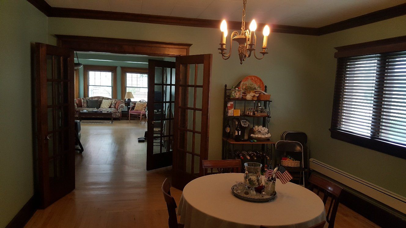Dining room with round table set for two, French doors lead to a sunroom, green walls, wood trim, chandelier.