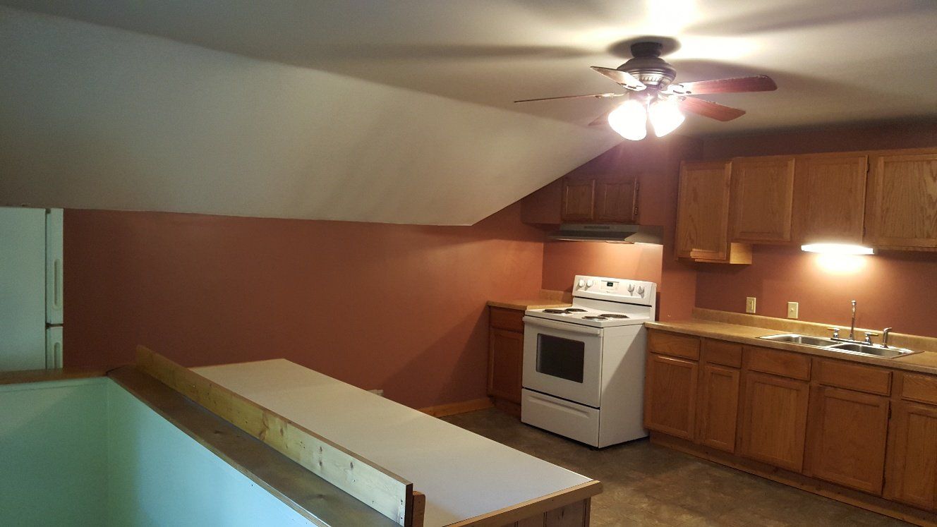 Kitchen with stove, cabinets, and a low barrier, under a sloped ceiling; brown and beige tones.