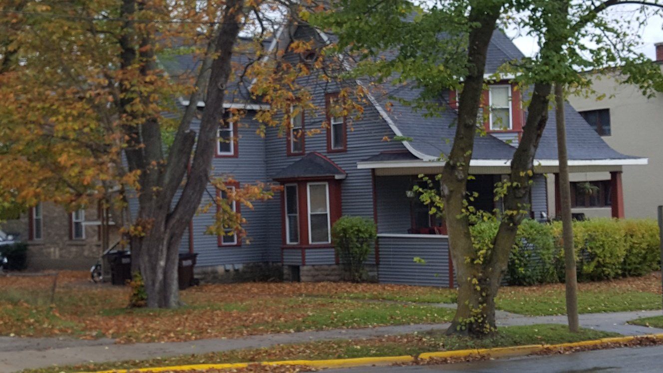 Blue, two-story house with gray roof, porch, and autumn trees in front.