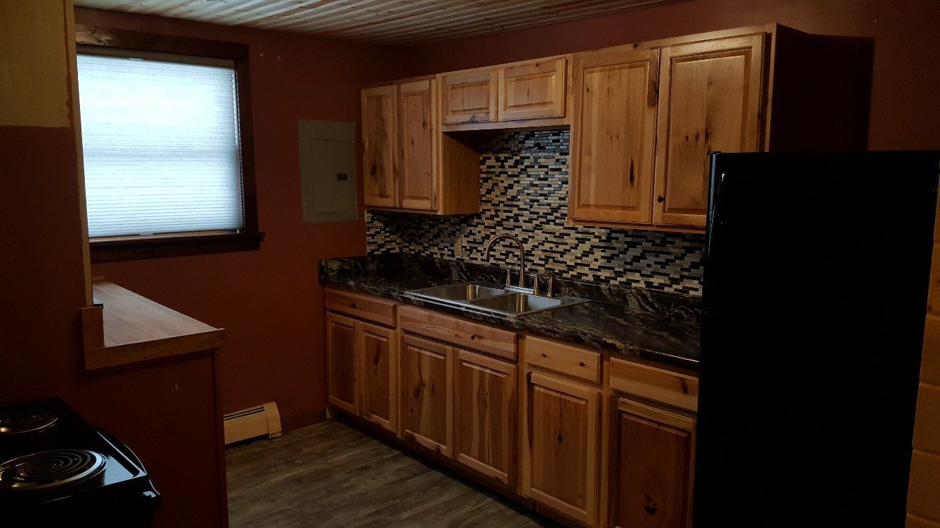 Kitchen with wooden cabinets, dark countertops, tiled backsplash, and black refrigerator.