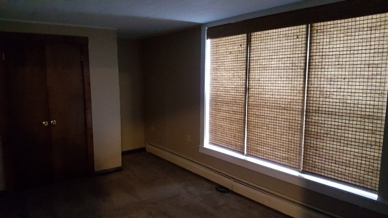 Empty room with a closet on the left, a window with woven shades on the right, and a radiator below.
