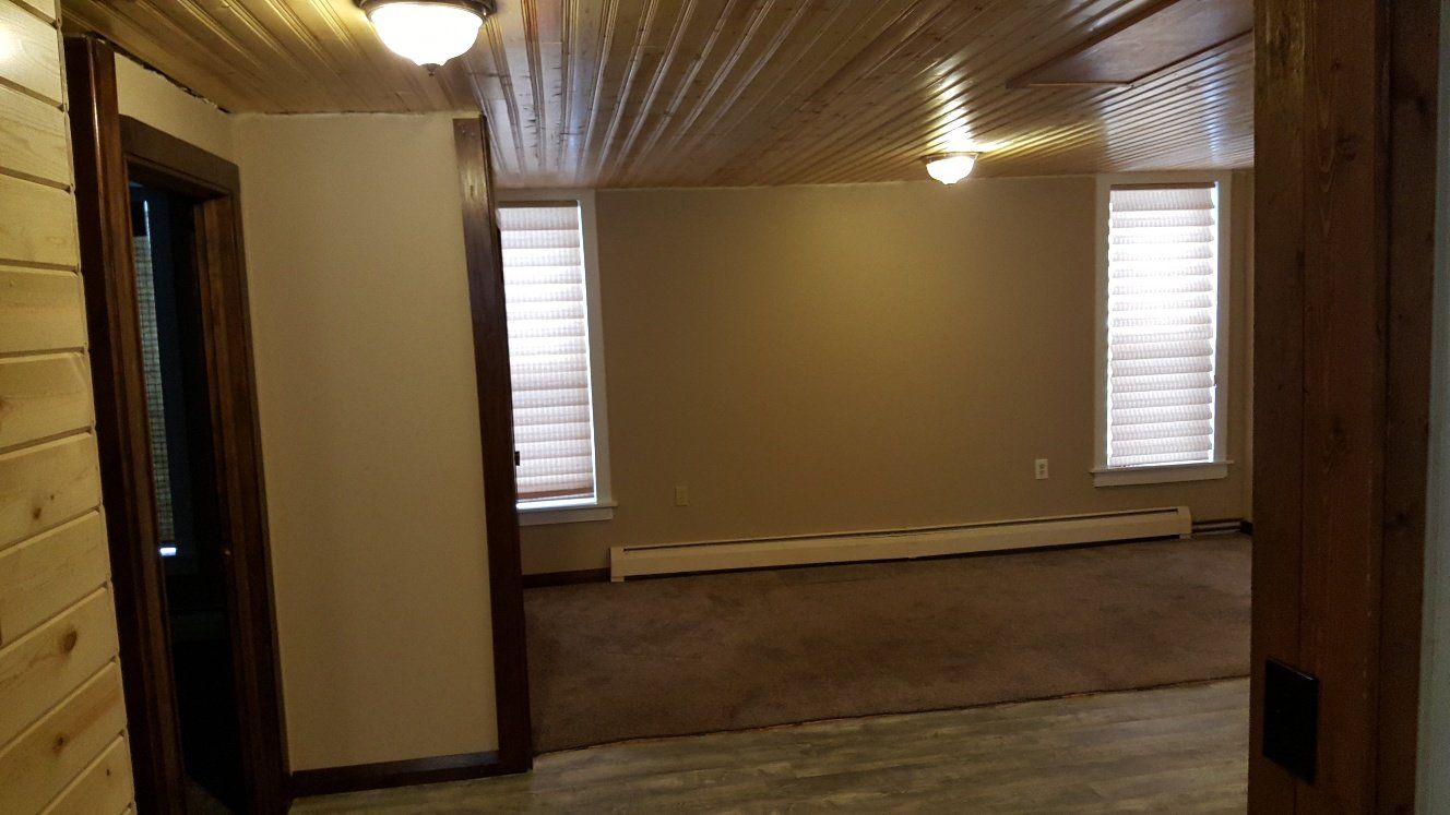 Interior room with brown carpet, two windows, and wood panel ceiling and trim.