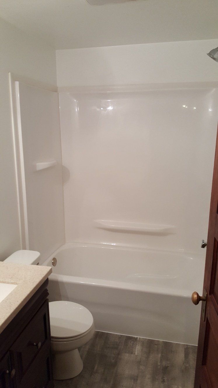 Bathroom with white bathtub/shower, toilet, dark vanity, and wood-look flooring.