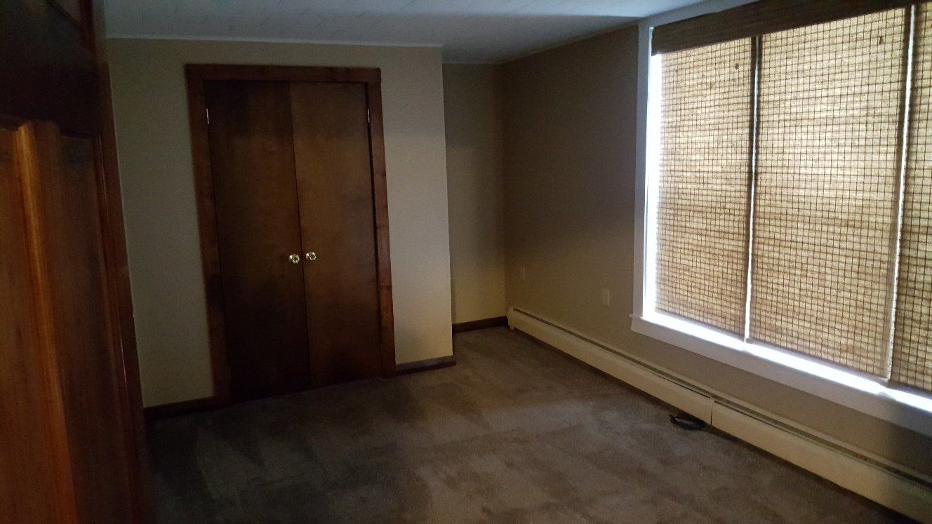 Empty bedroom with closet, window, and neutral-toned walls and carpet.