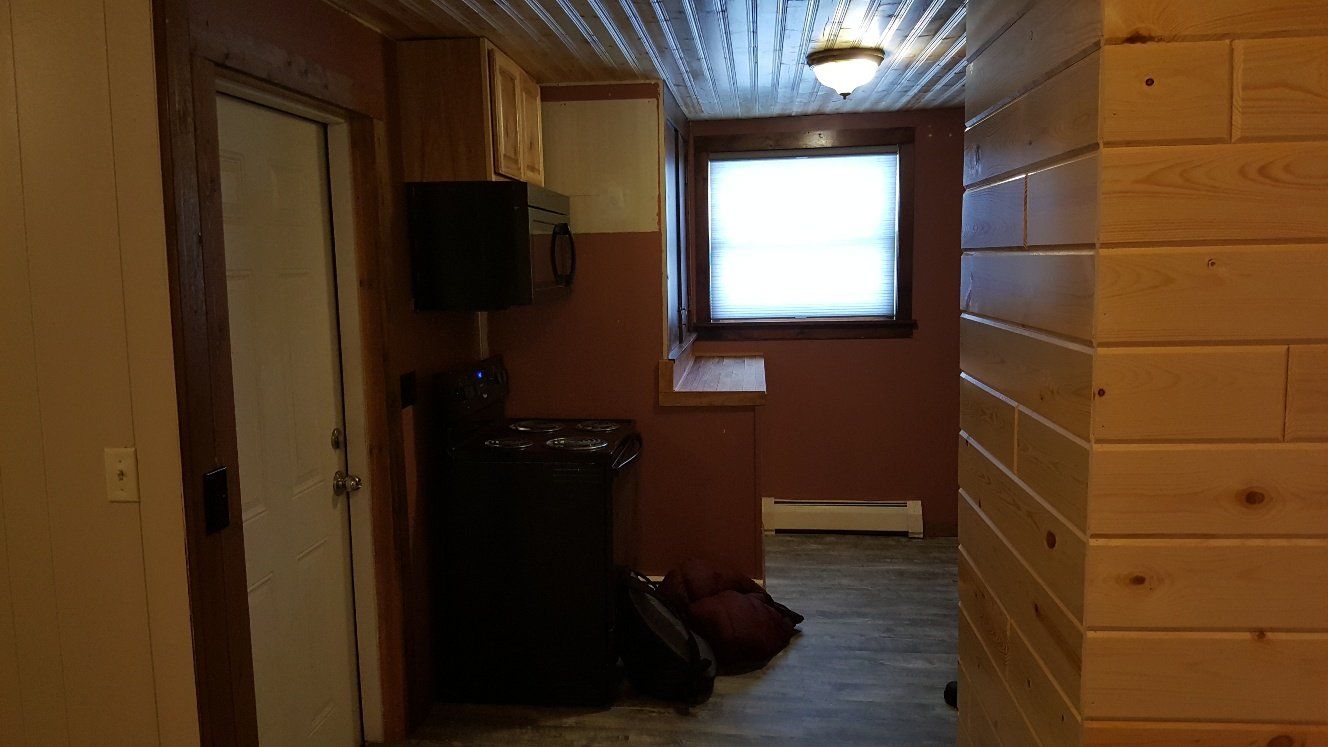 Interior hallway with wooden panel walls, window, door, and exposed corrugated ceiling.