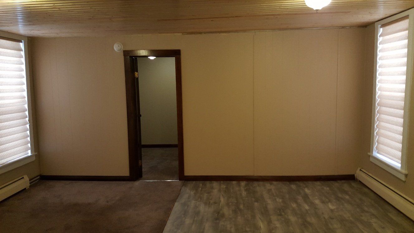 Empty room with two windows, doorway, tan walls, and carpeted floors.