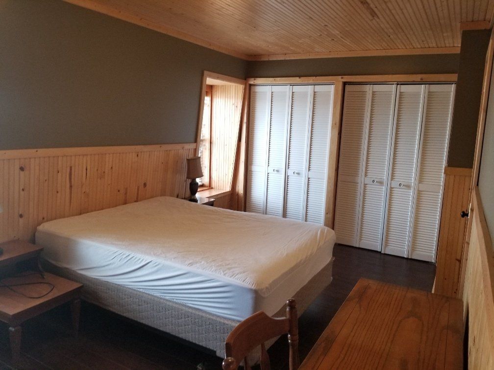 Bedroom with a bed, two closets, and wood paneling on the walls and ceiling.