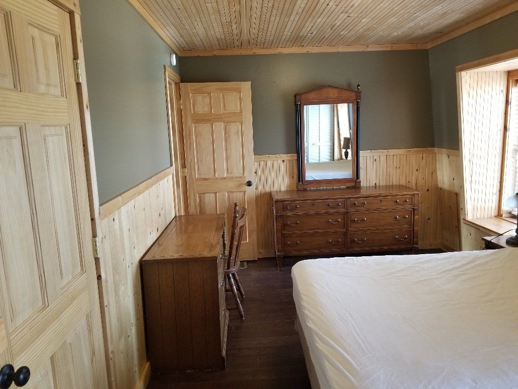 Bedroom with wooden paneling, a dresser with mirror, desk, and bed. Walls are green.
