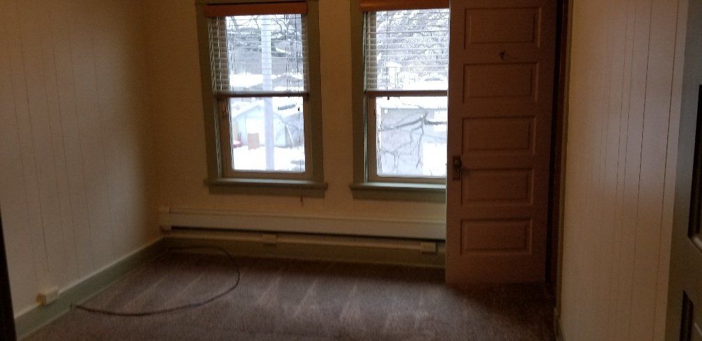 Empty room with two windows and an open door. Winter outside the windows; wood floor.