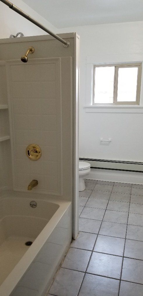 Bathroom interior with a shower/tub, toilet, window, and tiled floor.