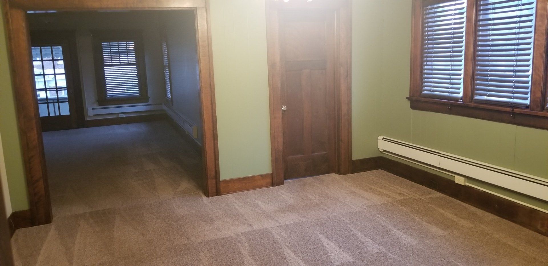 Room with green walls, brown trim, carpet, and a wooden door and window frames.