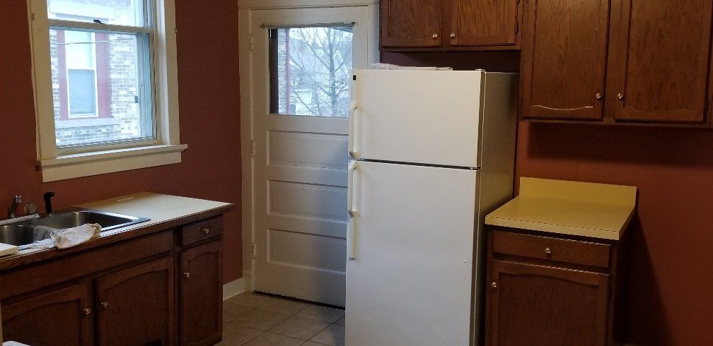 A kitchen with a refrigerator, cabinets, and a window.