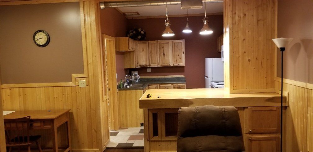 Interior with kitchen, brown walls, light wood paneling, countertops, bar with chair, and clock.