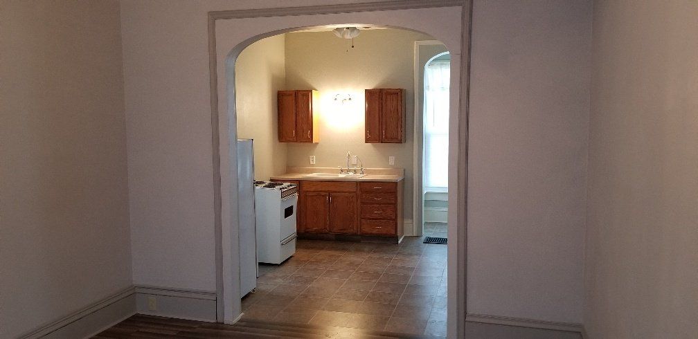 Interior view through an arched doorway of a kitchen with wood cabinets and a stove.