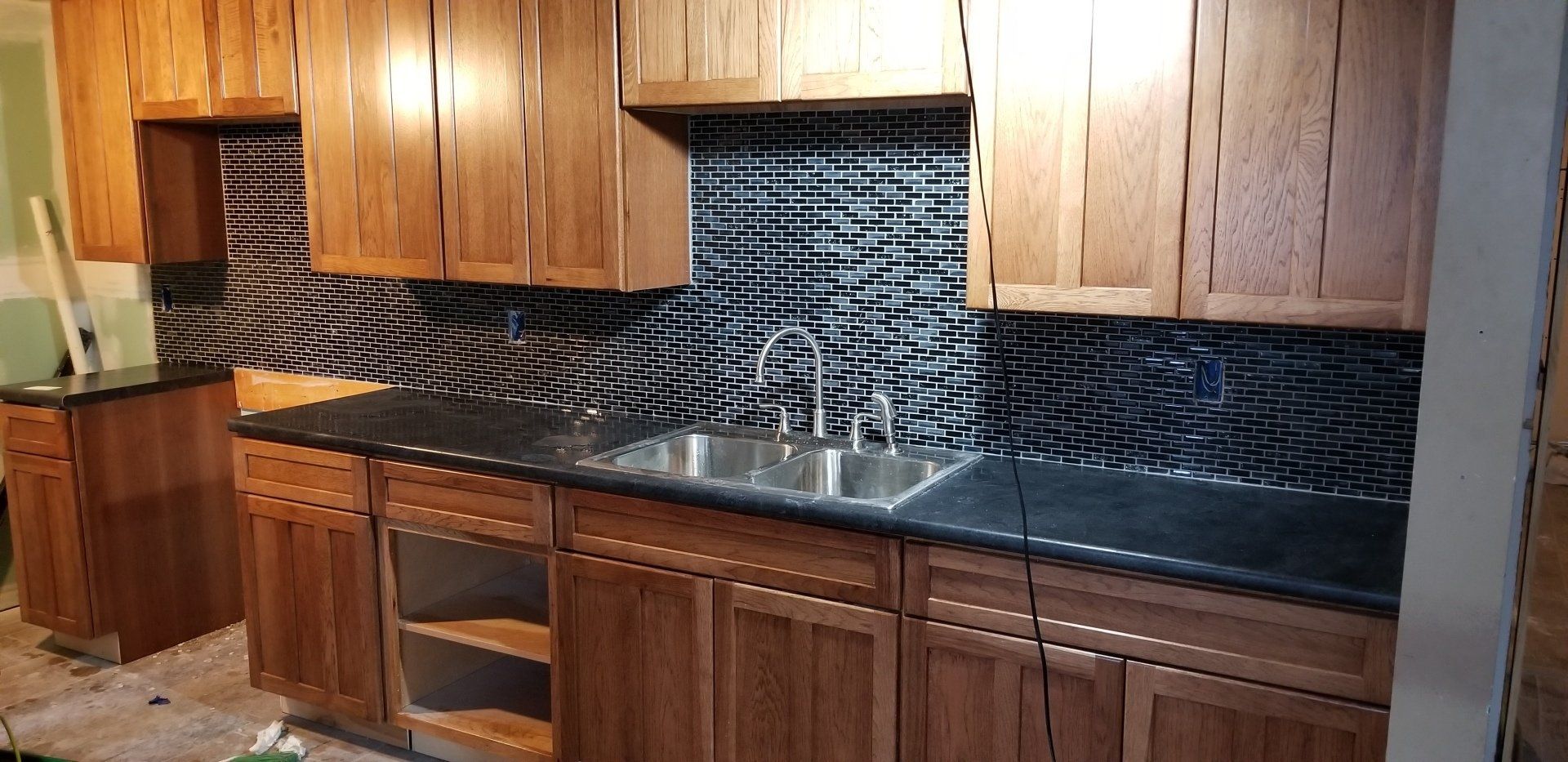 Kitchen renovation with wooden cabinets, dark countertops, and unique backsplash.