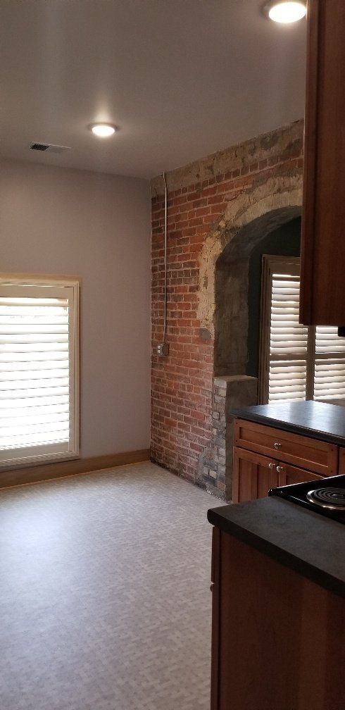 Interior view of a kitchen with exposed brick wall. Cabinets and a window with blinds are visible.